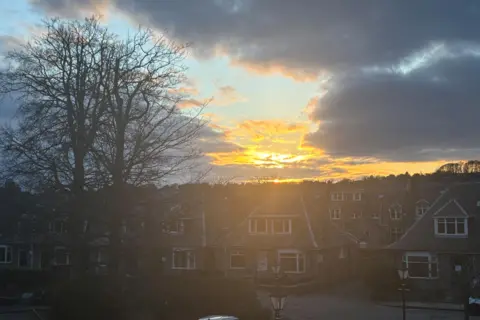 The glow of sunshine in the sky, behind clouds, over houses in Aberdeen.