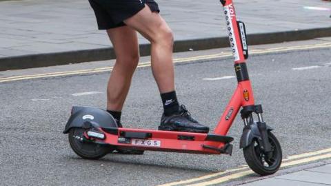 A persons legs on a voi e-scooter in the road