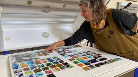 A woman points a finger at a table of coloured ceramic squares.