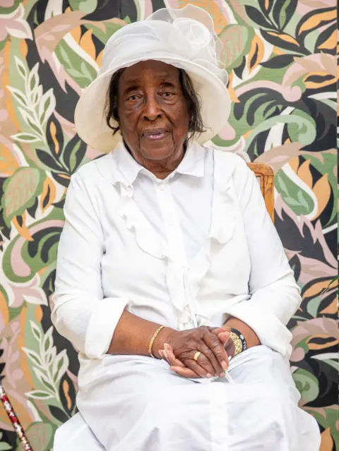 A woman sits in a chair wearing an all white outfit. 