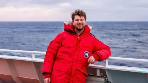 Jake Rosmarin wears a red puffer jacket on a boat