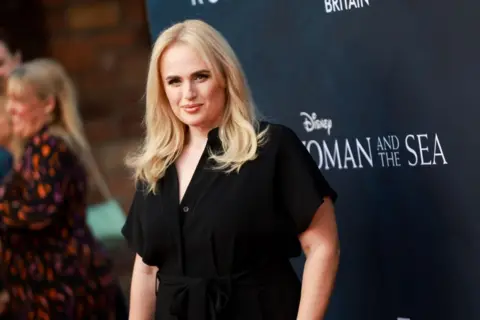 Getty Rebel Wilson, a young woman with blonde hair wearing a black jumpsuit, attends the Walt Disney Studios premiere of "Young Woman and The Sea" at The Hollywood Roosevelt on May 16, 2024 in Los Angeles, California.