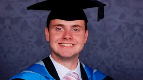 Jack O'Sullivan pictured in his blue graduation robes, wearing a black mortar board and smiling at the camera. 