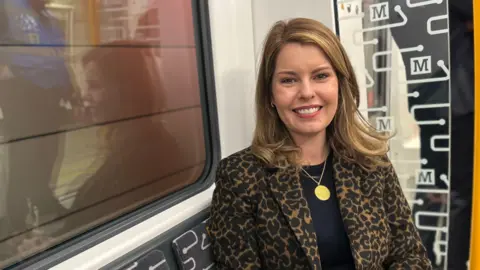 North East mayor Kim McGuinness on board the first new Tyne and Wear Metro train in passenger service. The interior is cream, black and yellow.  She has long blonde hair and is wearing an animal print blazer.