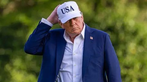 US President Donald Trump wearing a blue suit and a white cap with USA on it