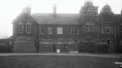 Essex Police A black and white picture shows a two-storey building with copious amounts of sandbags stacked in front of it.