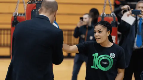 Coach Core Foundation A girl, wearing a black and green Coach Core t-shirt, thrusts her left hand towards a man in a suit in a punching action.