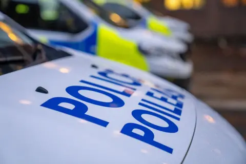 A police car parked with two other police cars out of focuse in the back ground. The words 'police' and 'poileas' are visible on the bonner of the main police car in the image. 