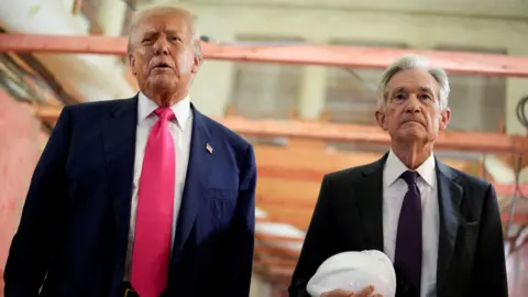Donald Trump appears next to Jerome Powell, who is carrying a white hard hat, during a visit to the Federal Reserve building as it undergoes renovations.