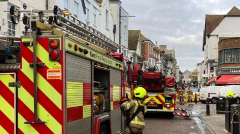 Two fire engines pictured near the former Debenhams store in Canterbury where a fire broke out on the night of Monday, 2 December. Three firefighters - one close, two further along to the right of the second fire engine - can be seen in the cordoned area.