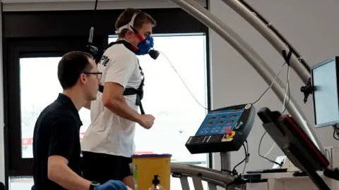 University of Worcester A man is on a running machine wearing a mask while another man looks a a screen carrying information. 