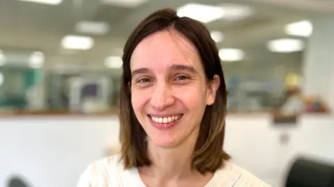 BBC/Martin Giles Dr Carolina Grandellis, who has shoulder-length brown hair, wearing a white button-up top in a laboratory.