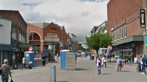 A busy paved shopping street with buildings on either side and a statue of a man in the centre