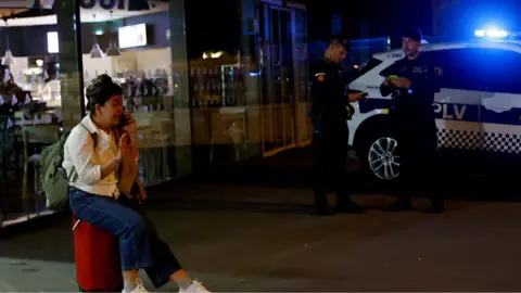 A woman speaks on the phone next to police officers at Joaquin Sorolla train station, as a power outage hit large parts of Spain, in Valencia, Spain, April 28, 2025. 