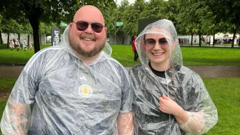 Two people wearing ponchos and smiling while standing in the pouring rain.