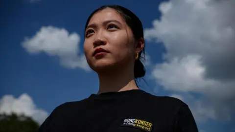 Anna Kwok photographed from below, hair tied into a bun, wearing a black t-shirt reading HONGKONGER