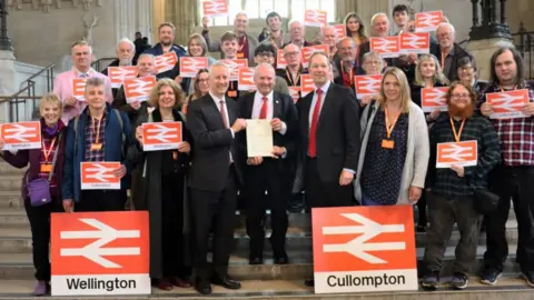 Richard Foord MP Campaigners for new railway stations in Wellington and Cullompton in Westminster including Gideon Amos MP (left) and Richard Foord MP (right) presenting a letter to Lord Hendy (centre)