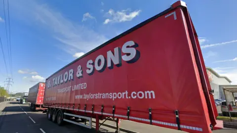A red lorry trailer with large red writing which reads: "B Taylor & Sons Transport Limited".