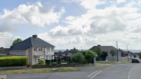 Google A road junction with houses and cars in the background.