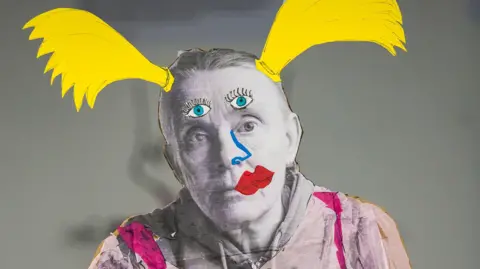 Black and white cardboard cut-out of writer and artist Lucy Edkins with added colourful pigtails, eyes and lipstick