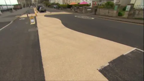 Wavy road markings, which are a pale brown colour, painted on a black road