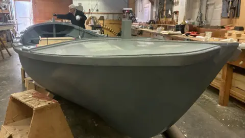 A grey moulded replica spy boat in a workshop