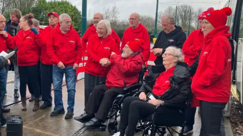 A choir group wearing red hoodies at the tram depot in Nottingham for the unveiling of a newly named tram 