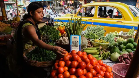 NurPhoto via Getty Images A  vegetable vendor waits for customers, displaying a barcode for Paytm, an Indian cellphone-based digital payment platform, at a market in Kolkata.