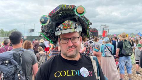 Man with massive pyramid stage hat on his head at Glastonbury