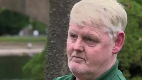 Handout A man in his 50s with sandy hair and a green-collared shirt looks to the side of the camera.