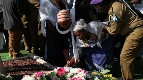 Reuters, a mãe do soldado israelense, o sargento Shahar Manoav é assistido enquanto lamenta o túmulo do filho, durante seu funeral em Ashkelon, Israel (25 de junho de 2025)
