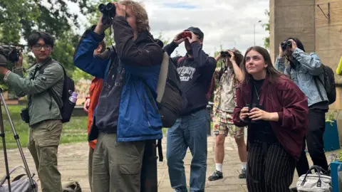 BBC/Simon Thake A group of young people holding binoculars are gazing at something off screen