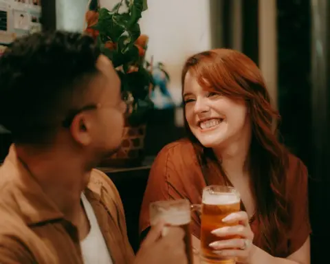 Ippei Naoi/Getty Images A young man and woman hold up pints of beer in a pub and smile