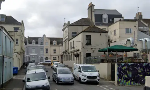 Google Maps Google Maps image of Moor View Terrace. Cream buildings are built on either side of the narrow side street. A number of cars and vans are parked on either side of the road. 