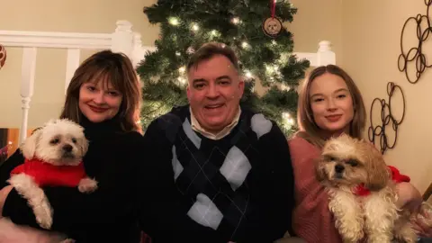 Two women sit and hold dogs on either side of a man 