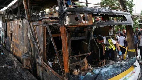 Reuters Inspectors work inside a burnt-out bus that caught fire while carrying teachers and students from Wat Khao Phraya school, reportedly killing and injuring dozens, on the outskirts of Bangkok, Thailand, October 1, 2024. 