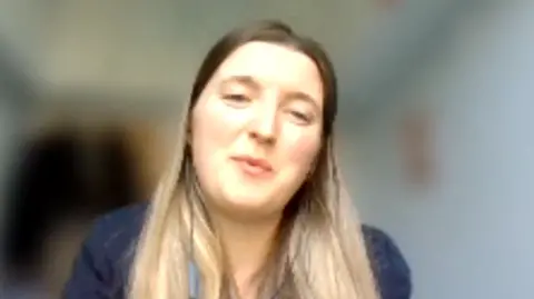 Juliette Flach looks at the camera during an online video call. She has long brown hair and a navy top