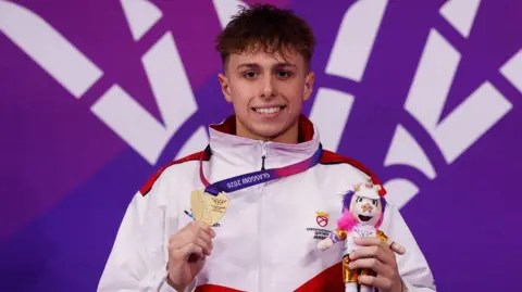 Reuters Filip Nowacki sostiene su medalla de oro y una pequeña mascota de peluche, y sonríe. Tiene el pelo corto, oscuro y rizado, y lleva un anorak con el logo del equipo.