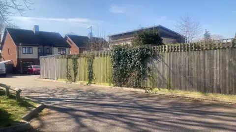 Part of Stanesfield Road in Cambridge. The road is part of a residential area with fencing and trees. 