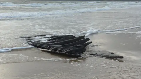 National Trust The blackened timbers are pictured at high tide in Studland Bay. The tide is lapping water over the remains. 