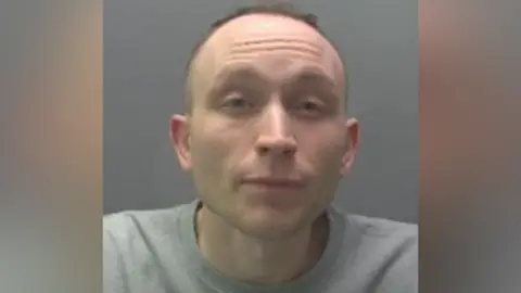 Custody image of Gregory Coulson - he is wearing a grey jumper and his hair is receding