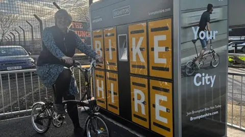 Wychavon District Council Councillor Beverley Hardman is on one of the bikes next to the dock. There are railings around it.