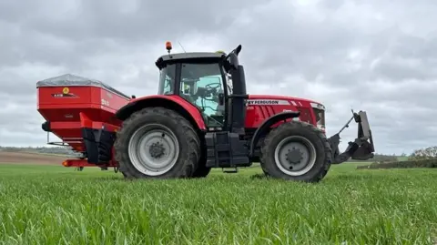 Janine Machin/BBC A large red tractor parked on a green field under leaden skies.