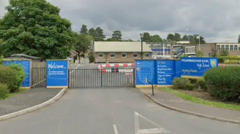 Google Blue signage surrounds the school gates to a low level brick building, driveway and two-storey modern building on the right of the photo.