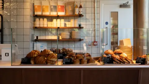 Louis Alder Tap Socials’s bakery products on display at Day Release at Milton Park’s Signal Yard. Some plates, cups and coffee bags are seen on the shelves behind.