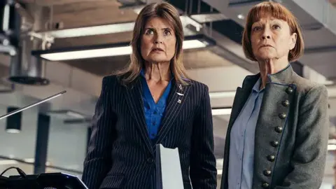 James Pardon/BBC A woman in a pinstripe suit next to another in a buttoned military style coat both looking ahead seriously - from Power of the Doctor 2022