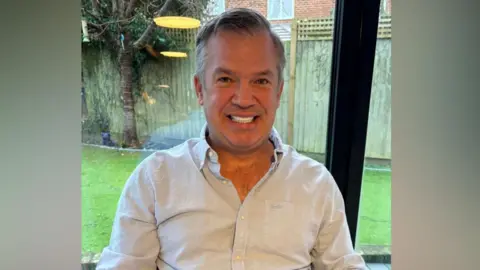 Kent Police A middle-aged man in a shirt with the top buttons undone smiles. 