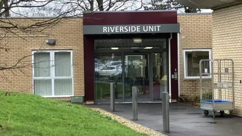 The entrance to Riverside Adolescent Mental Health Unit is pictured with glass sliding doors set in a yellow brick one storey building