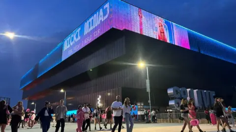 Reuters People walk away from a large music venue. A picture of Nicki Minaj is projected onto the top.