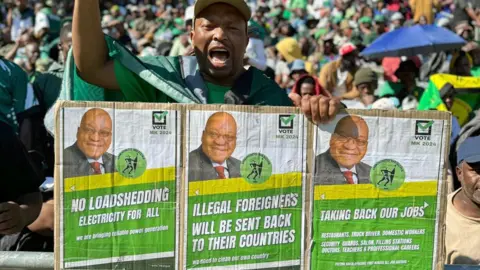 Ed Habershon/BBC A supporter of Jacob Zuma holding up small posters with MK pledges